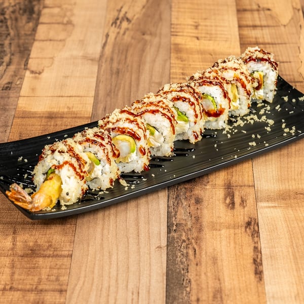 A long black plate holds a row of sushi rolls with shrimp tempura, avocado, and sauce.