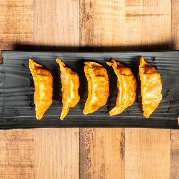 Five golden-brown fried dumplings are arranged on a black rectangular plate on a wooden table.