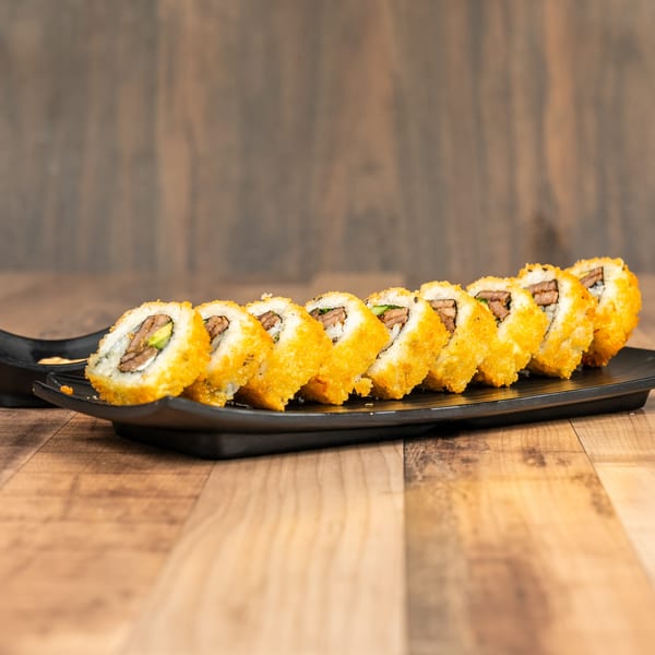 A black rectangular plate holds a row of golden-fried sushi rolls with beef and avocado.