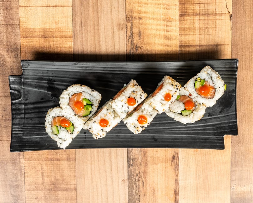 Sushi rolls with salmon, cucumber, and orange sauce on a black rectangular plate.