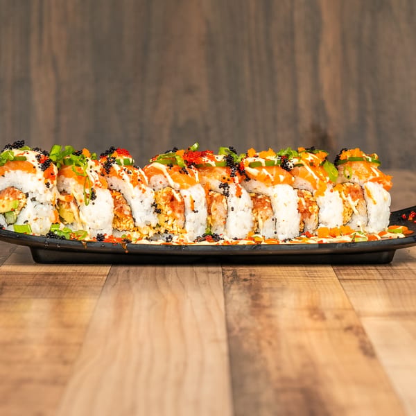 A long platter of sushi rolls topped with salmon, roe, green onions, and sauces.
