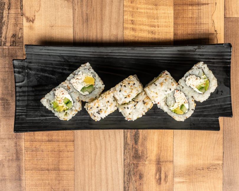 Six pieces of sushi with rice, avocado, and crab meat on a black rectangular plate.