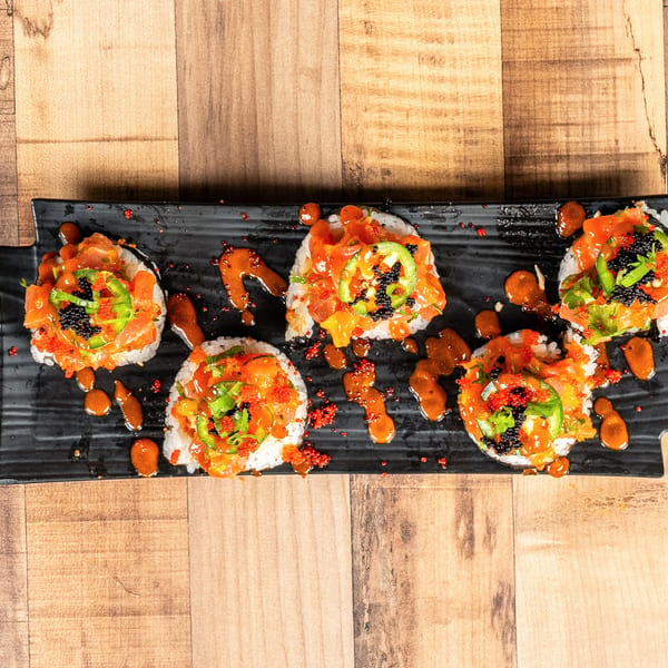 Five sushi rolls with salmon, green peppers, and roe on a black plate.