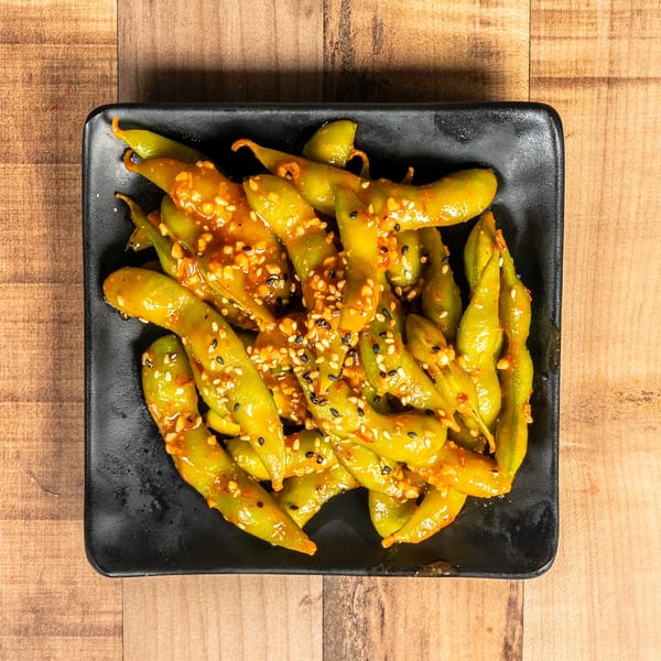 Spicy edamame with sesame seeds in a black rectangular dish on a wooden table.