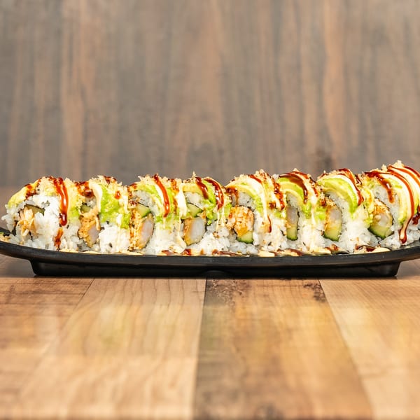 Sushi roll with avocado, shrimp tempura, and sauces on a black plate, on a wooden table.
