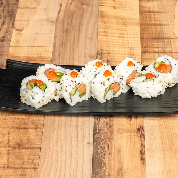 Salmon and cucumber sushi rolls with orange sauce on a black rectangular plate.