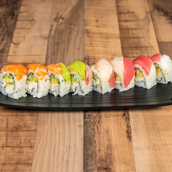 A black rectangular plate holds a row of sushi rolls with various colorful toppings on a wooden table.