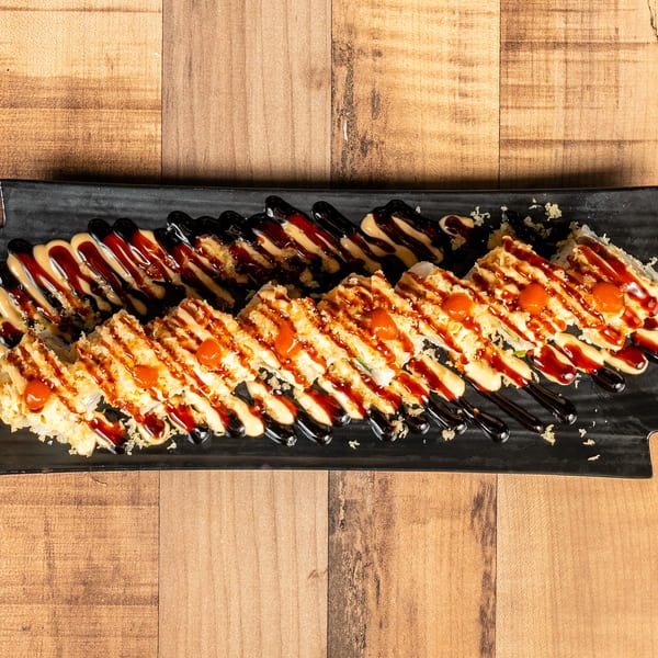 A black rectangular plate filled with sushi rolls, drizzled with dark and light sauces, on a wooden table.