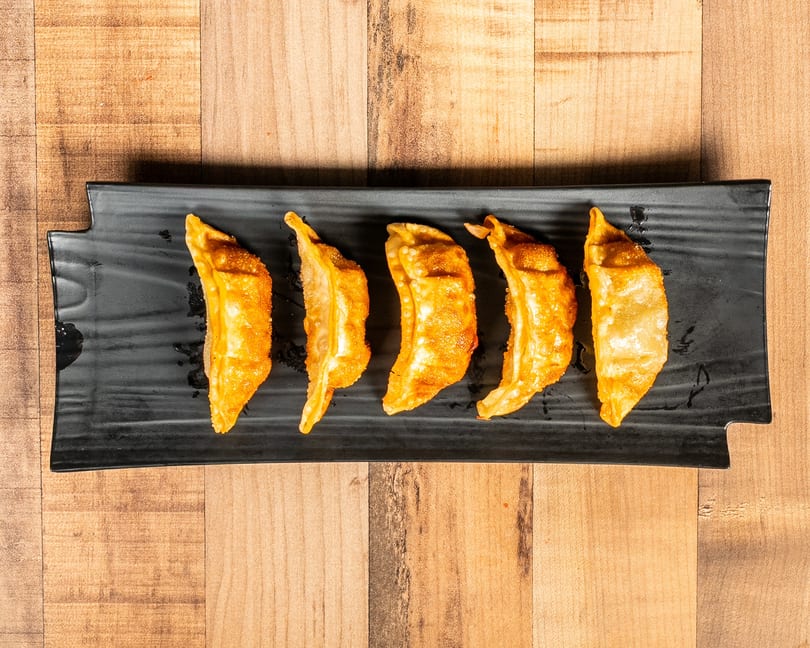 Five golden-brown fried dumplings are arranged in a row on a black rectangular plate.