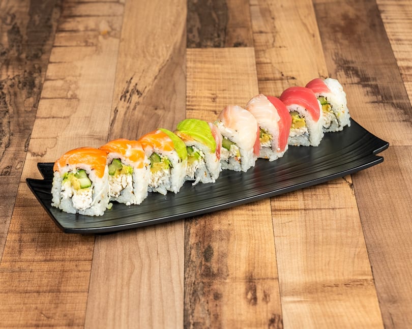 Colorful sushi rolls with salmon, avocado, tuna, and white fish on a black rectangular plate.