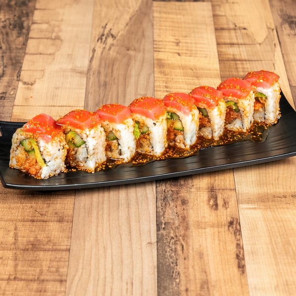 A row of sushi rolls with tuna, avocado, and cucumber, drizzled with sauce and roe.
