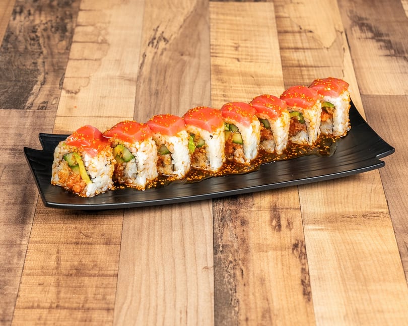A row of sushi rolls with tuna, avocado, and cucumber, drizzled with sauce and roe.